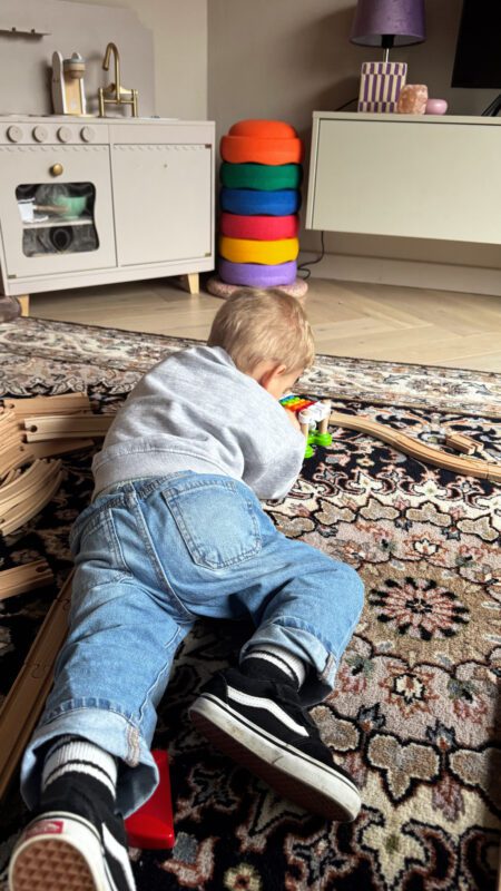 Peuter zelfstandig spelen met een houten trein en stapelstein erachter.